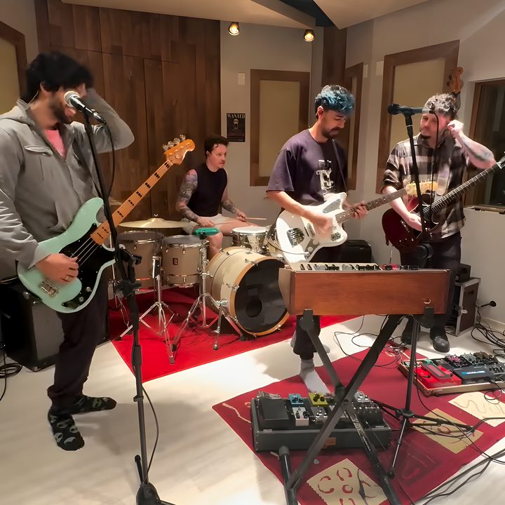 Os integrantes da Kool Kids tocando juntos no estúdio, com baixo, bateria e duas guitarras.